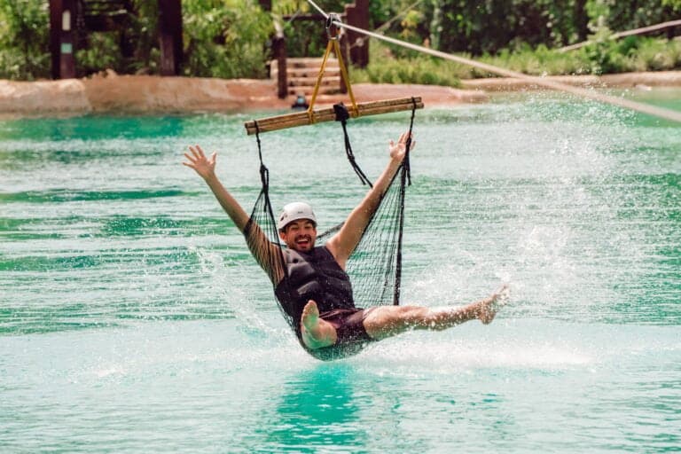 Un hombre sonriente montando en un columpio de tirolesa y salpicando en una laguna de agua turquesa en Scape Park Cap Cana.
