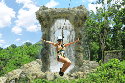 Una mujer disfruta de un emocionante paseo en tirolesa frente a una cascada en Scape Park Cap Cana.