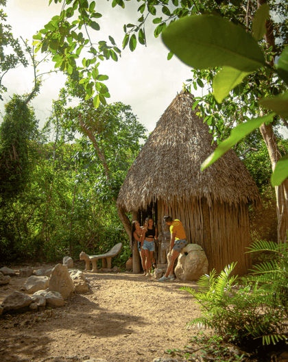 Visitantes exploran una choza tradicional taína y exhibición cultural rodeados por la frondosa selva en Scape Park Cap Cana.