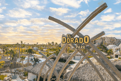 Gran estructura de madera con el letrero de El Dorado Park que domina un parque acuático tropical con cabañas de techo de paja bajo un cielo nublado.
